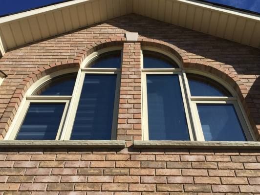 Brick building with arched windows, beige frames, and blue-tinted glass against a blue sky.