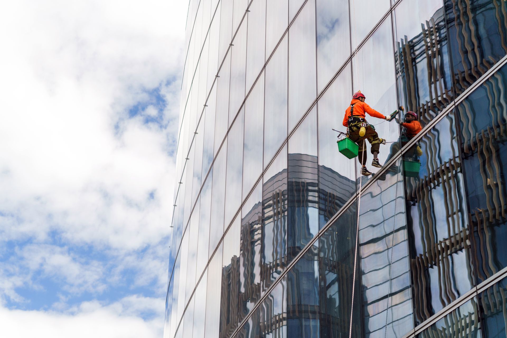 Two window cleaners in orange gear rappelling on a glass office building