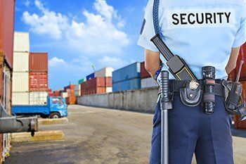 Security guard standing in a shipping yard beside stacked cargo containers and a truck