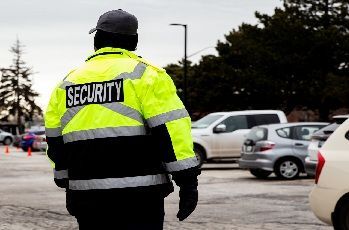 High-visibility security guard walking through a parking lot with cars in the background