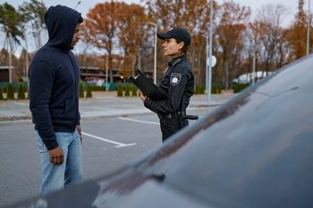 Police officer talking to a hooded person beside a car in a parking lot