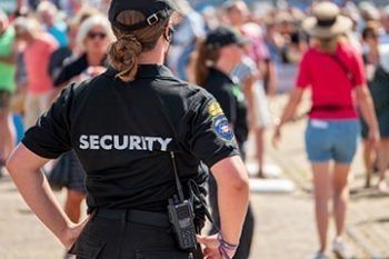 Security officer in black uniform standing with hands on hips in a crowded outdoor area