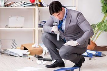 Technician kneeling on floor inspecting a damaged pipe in a cluttered office space