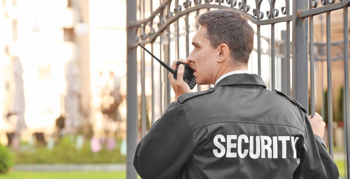 Security guard in black jacket using a walkie-talkie by a gated entrance