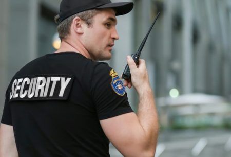 Security guard in black shirt and cap holding a radio on a city street