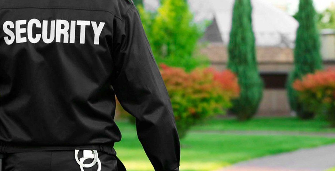 Security guard in black uniform standing outdoors near a lawn and building.
