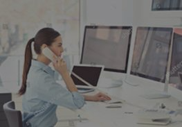 Woman on phone at a desk with multiple computer monitors in a bright office