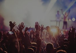 Crowd with raised hands at a concert, bright stage lights glowing in the background