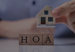 Hand placing a small house above wooden blocks spelling HOA