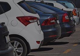 Rear view of parked cars in a lot, including white, blue, and black vehicles