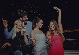 Four friends dancing and smiling at a party, holding drinks with confetti falling around them