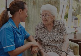 Nurse in blue talking with an elderly woman on a porch, holding her hand