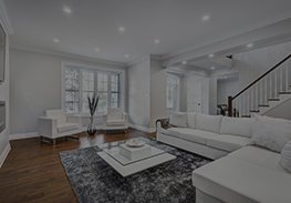 Bright modern living room with white sectional sofa, coffee table, hardwood floors, and staircase.