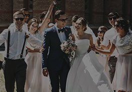 Wedding party walking outdoors, with bride and groom centered and guests smiling around them.