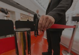 A person pulling a red stanchion rope on a red-carpeted entrance path with a crowd behind.