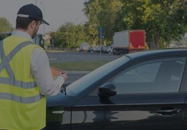 Traffic officer writing a ticket beside a black car on a roadside