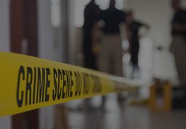 Yellow crime scene tape across a blurred indoor scene with police officers in the background