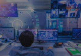 Person viewing multiple monitors in a blue-lit control room, monitoring data on screens.