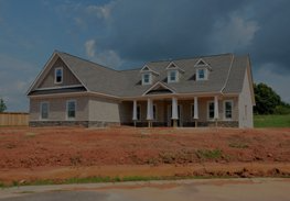 New gray house under construction with a front porch and red dirt yard under a blue sky