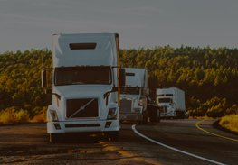 Three white semi-trucks driving along a winding road at sunset