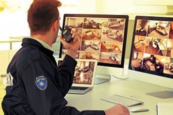 Security guard monitoring multiple surveillance screens in an office