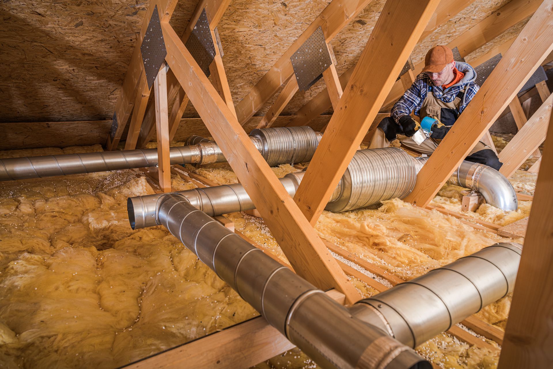 Attic crawl space with exposed ducts, wooden beams, insulation, and a worker on the right side.