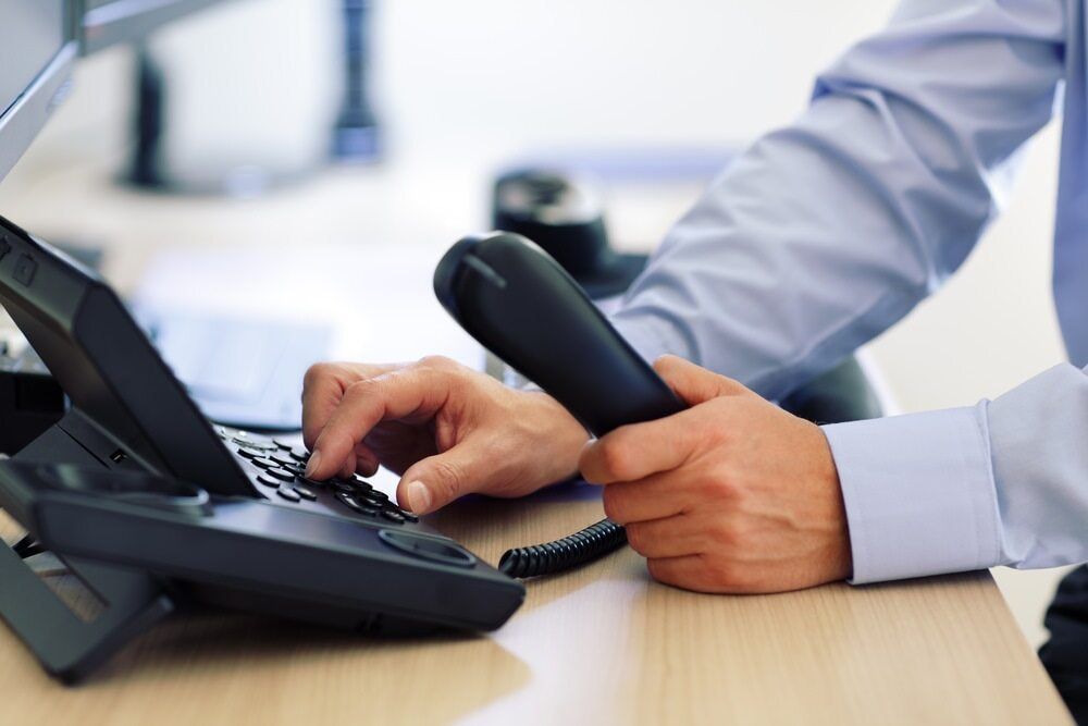 Person at a Desk Using a Black Office Phone, Dialing Numbers — Flexicoms Communications in Tully, QLD