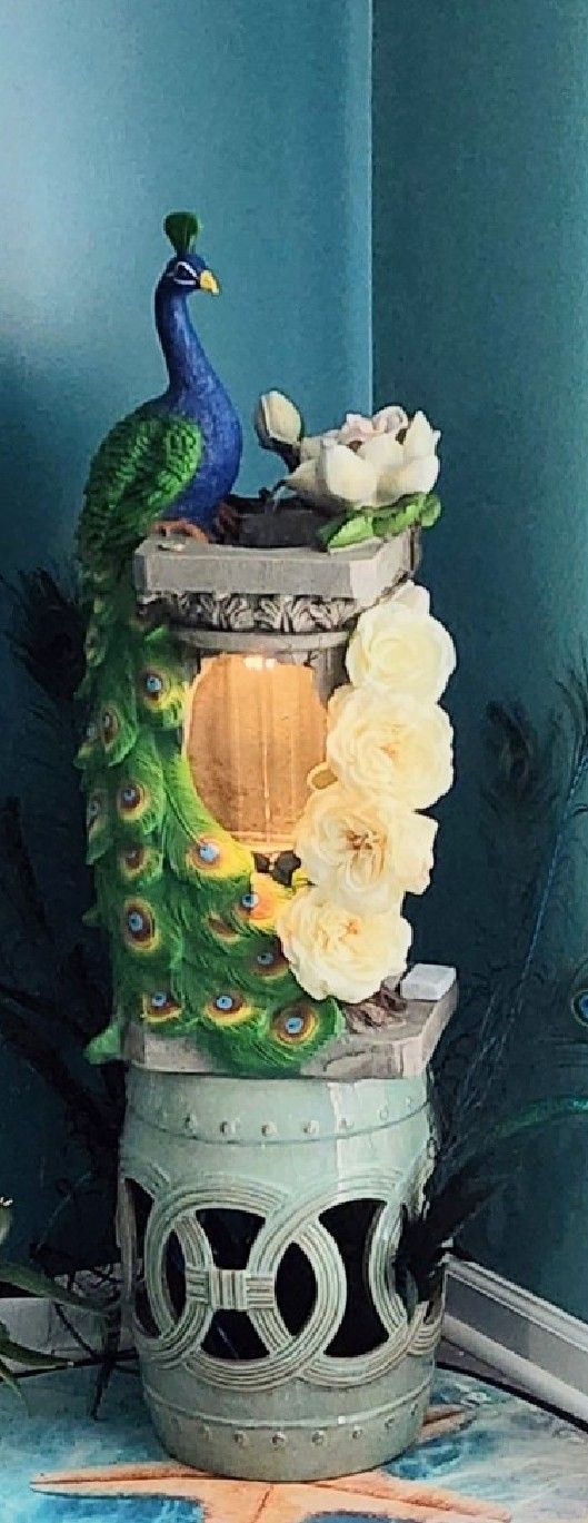 A peacock is sitting on top of a candle holder with flowers.