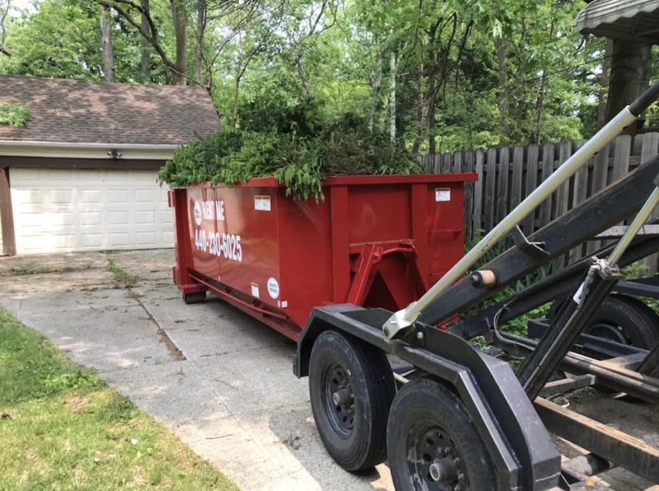 a red dumpster is sitting on a trailer in front of a garage .