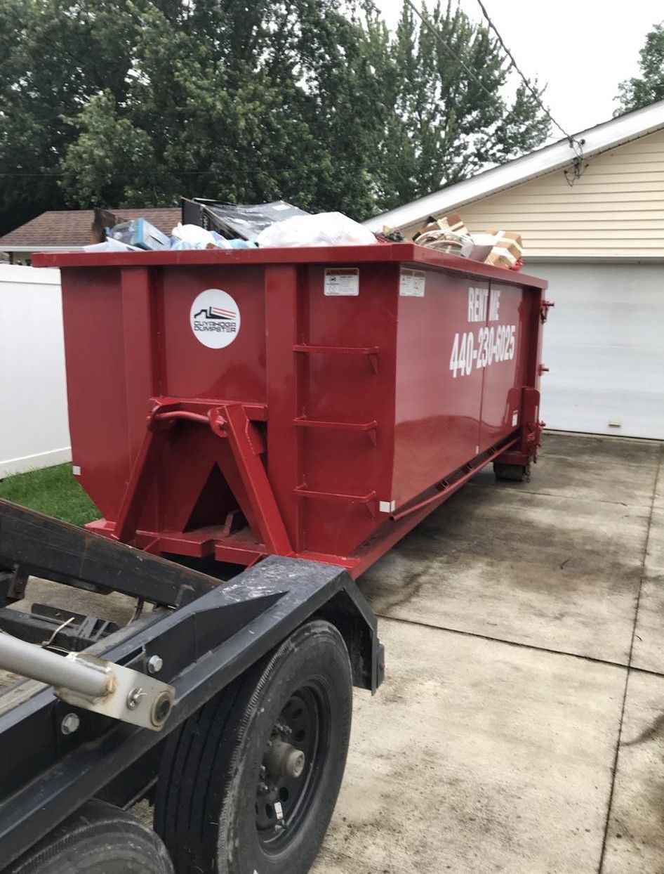 a red dumpster is sitting in a driveway next to a trailer .
