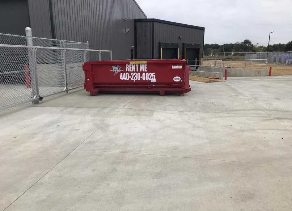 a large red dumpster is sitting in a parking lot next to a chain link fence .