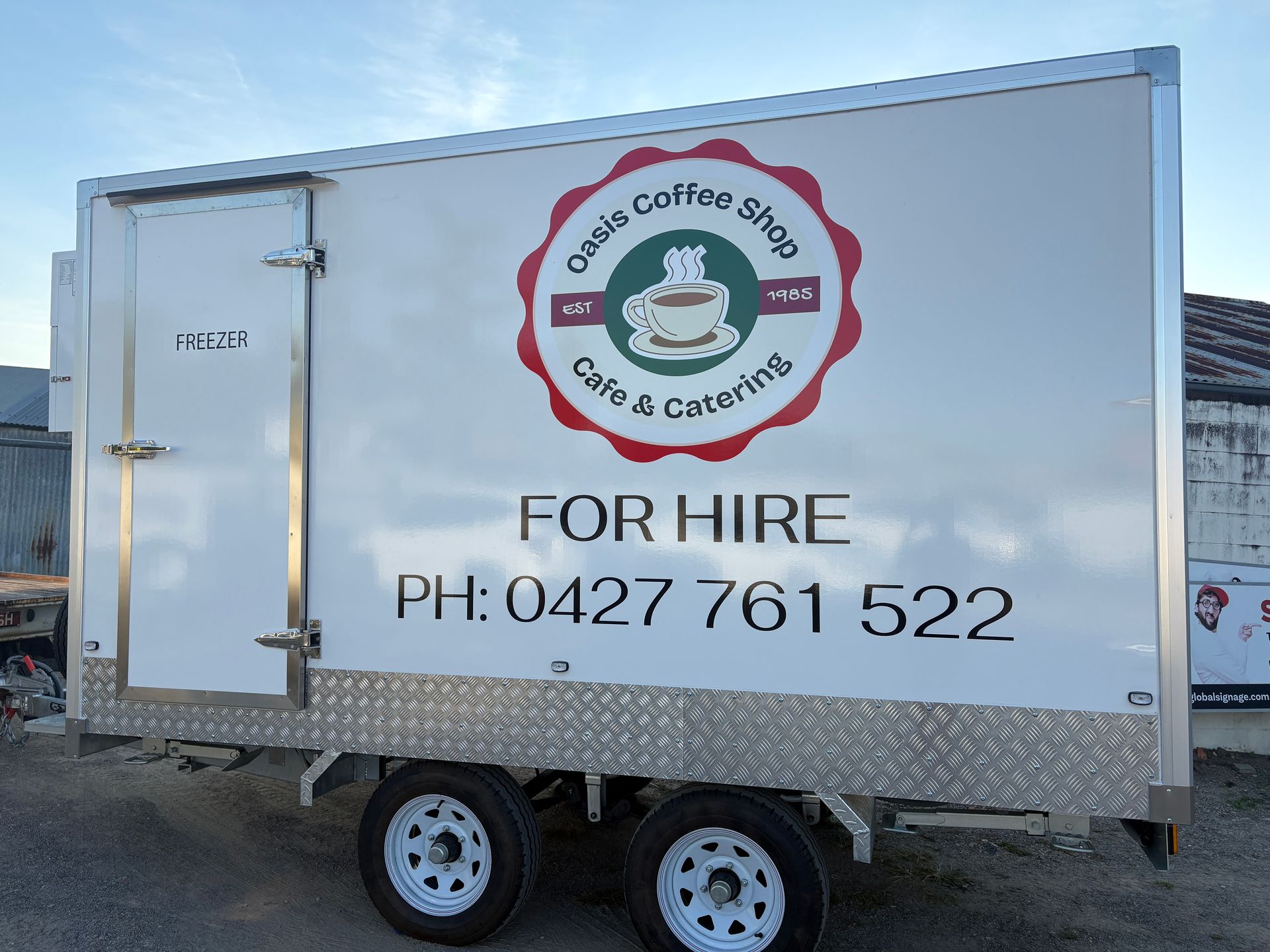 A white boat is parked on a trailer next to a body of water — Global Signage In Ingham, QLD
