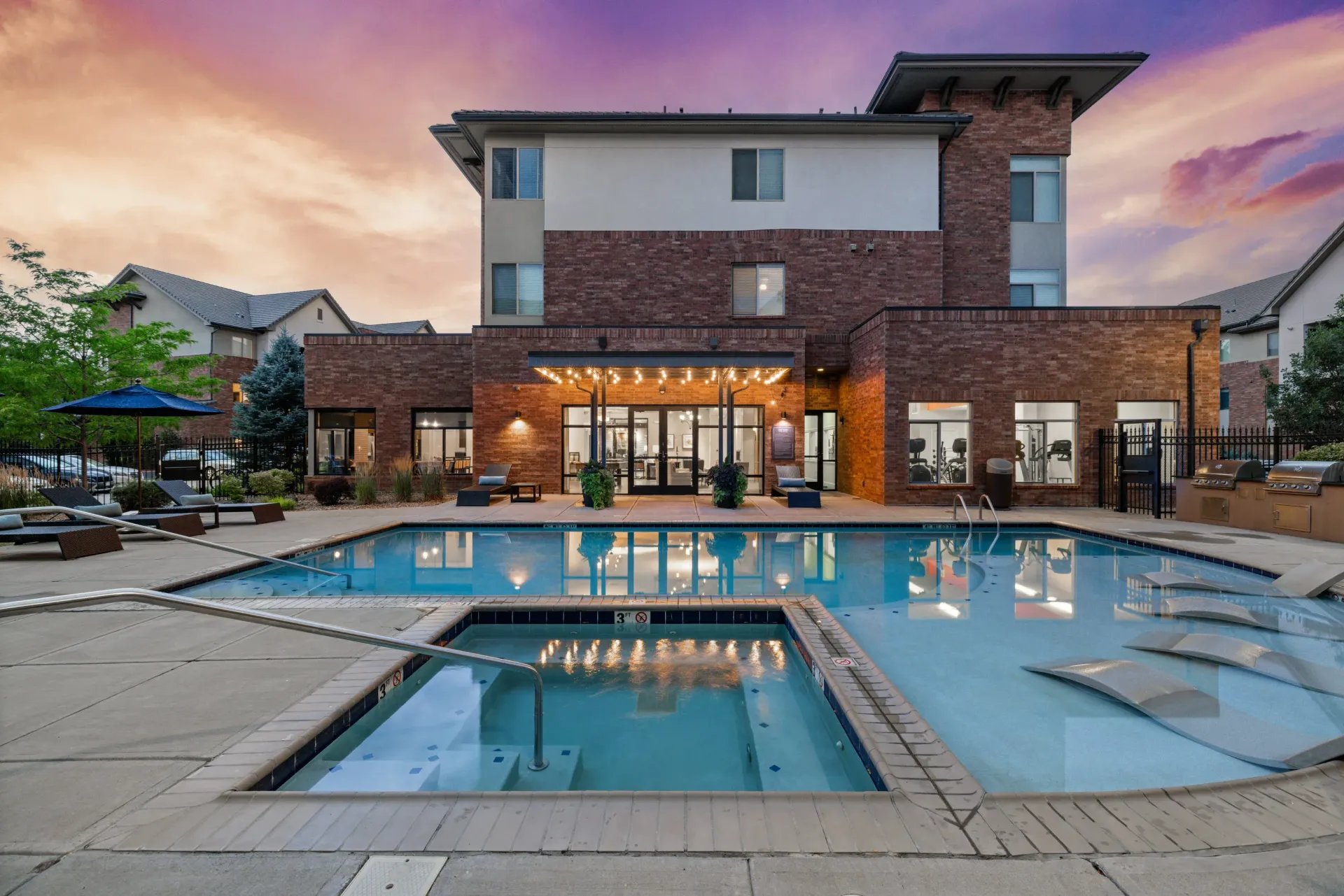 Exterior view of a brick apartment pool area with lounge chairs at sunset at The Parc at Greenwood Village.
