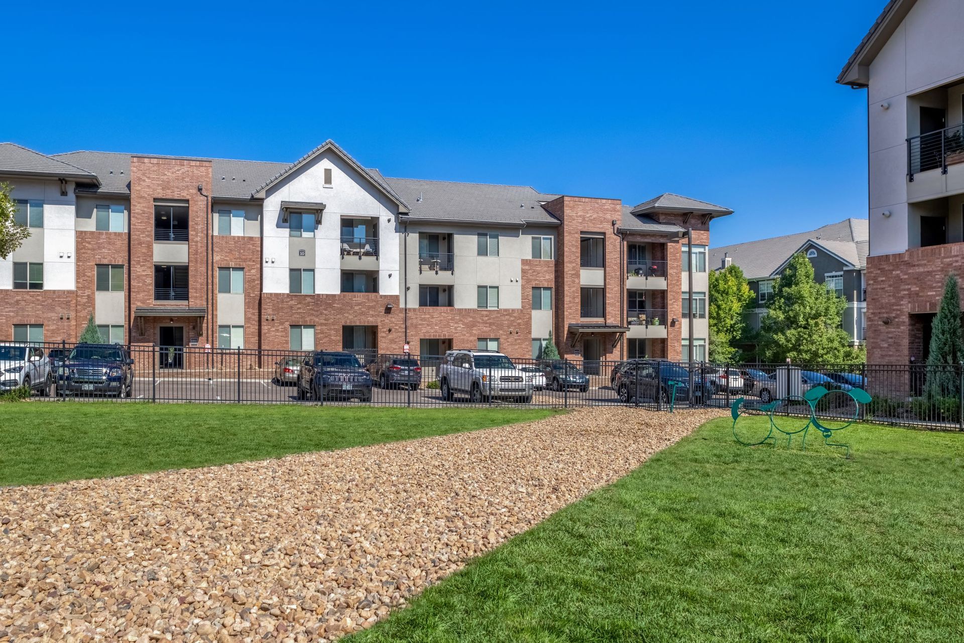 Exterior view of a multi-building apartment community with parking and green lawn at The Parc at Greenwood Village.