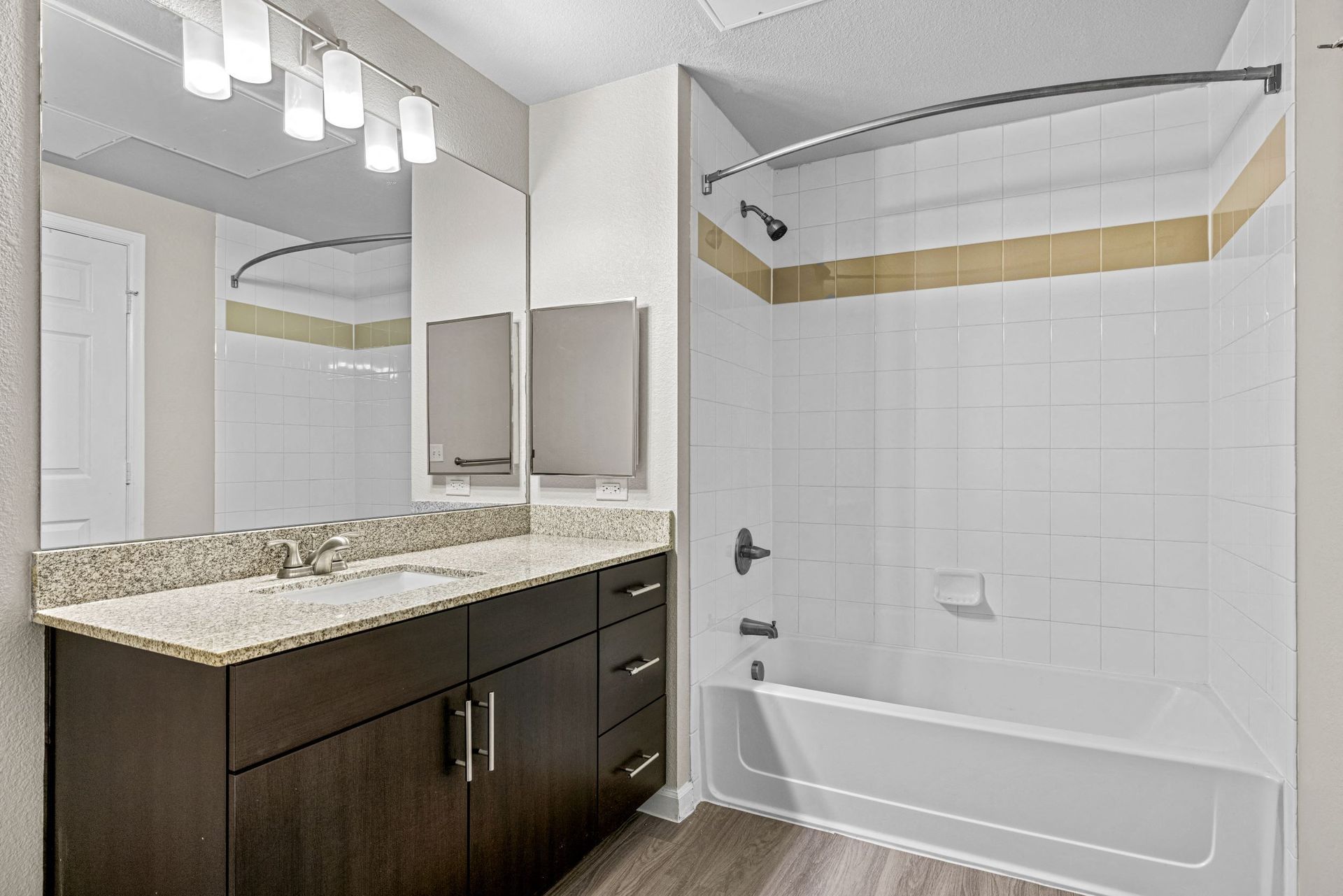 Bathroom with granite vanity, large mirror, and white tiled tub/shower in an apartment at The Parc at Greenwood Village.