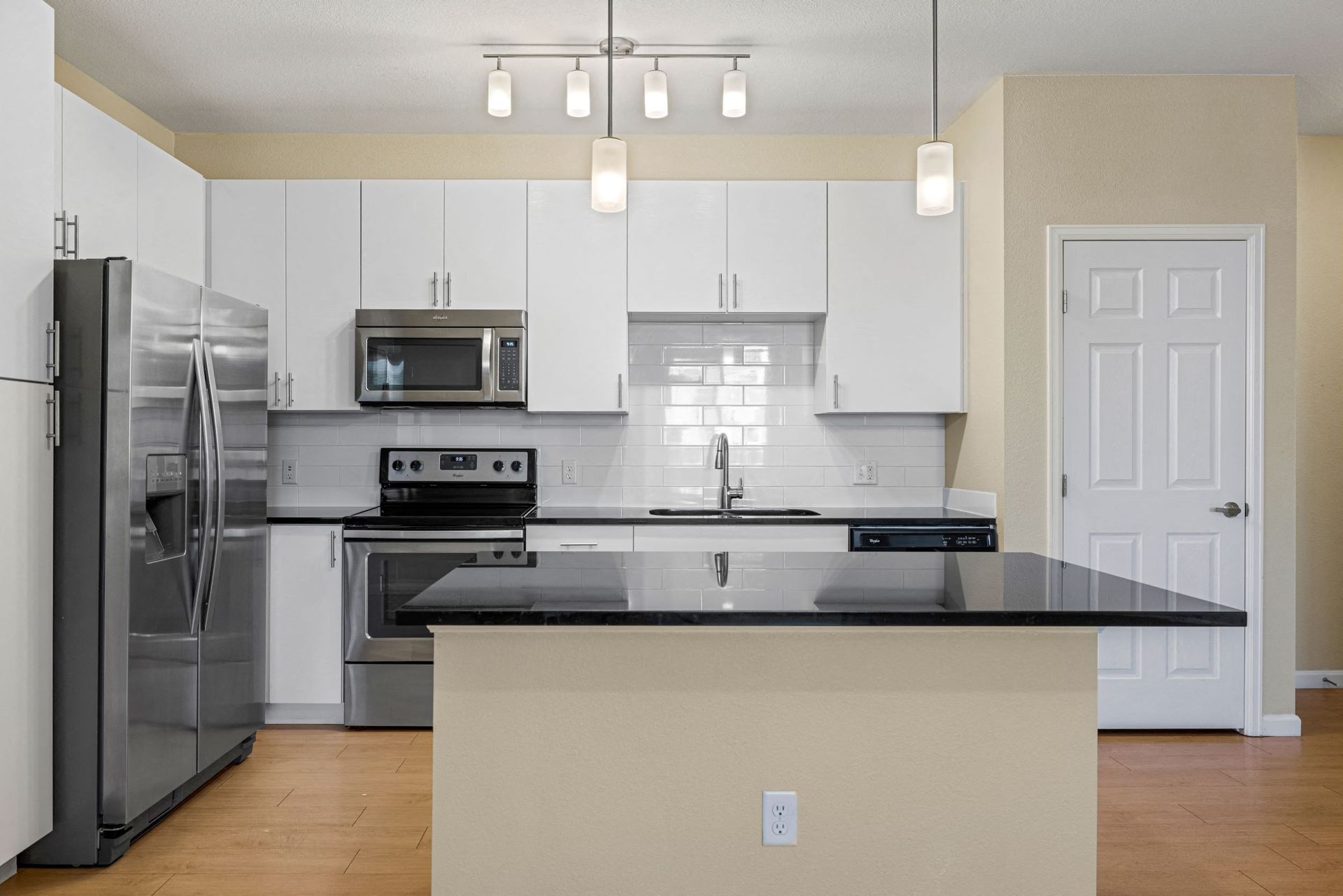 Kitchen in a modern apartment with white cabinets, stainless steel appliances, and a black island at The Parc at Greenwood Village.