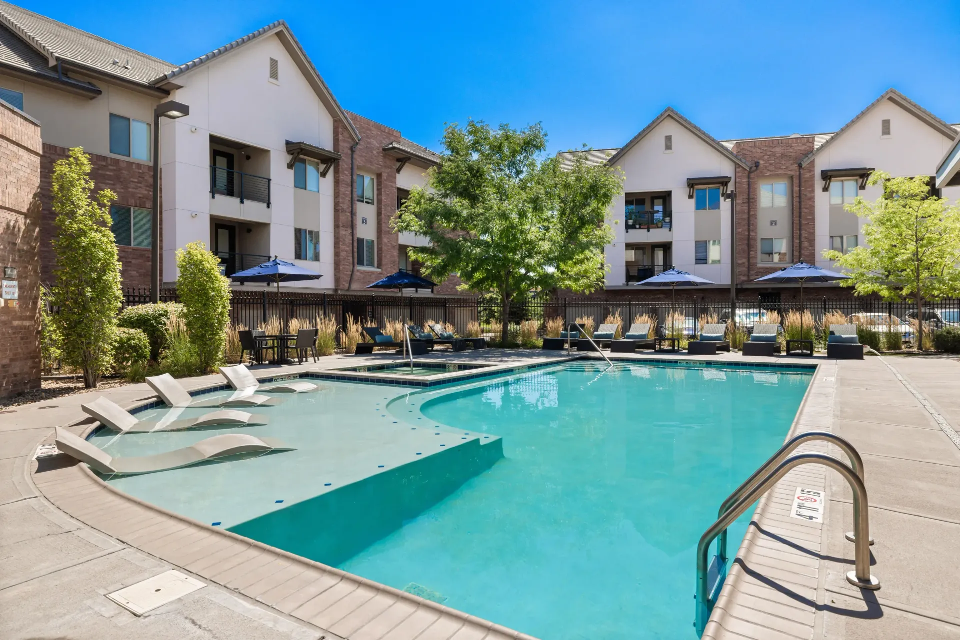 Outdoor community pool with lounge chairs and umbrellas in a landscaped courtyard at The Parc at Greenwood Village.