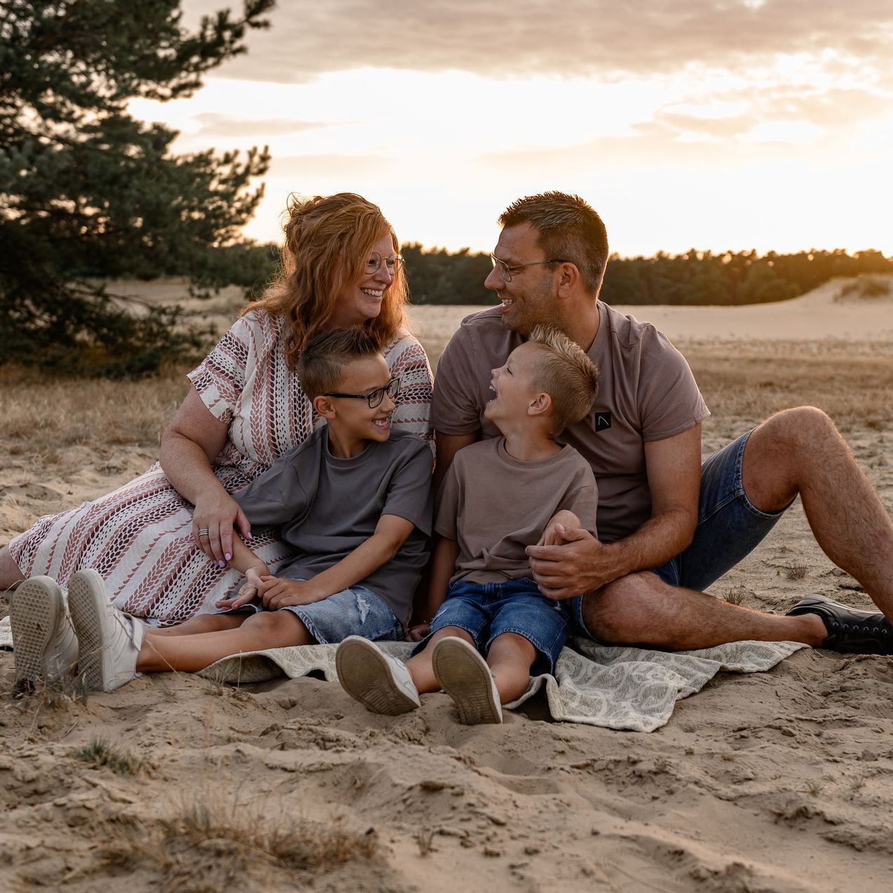 Een gezin van vier lacht terwijl ze tijdens zonsondergang op het strand zitten.