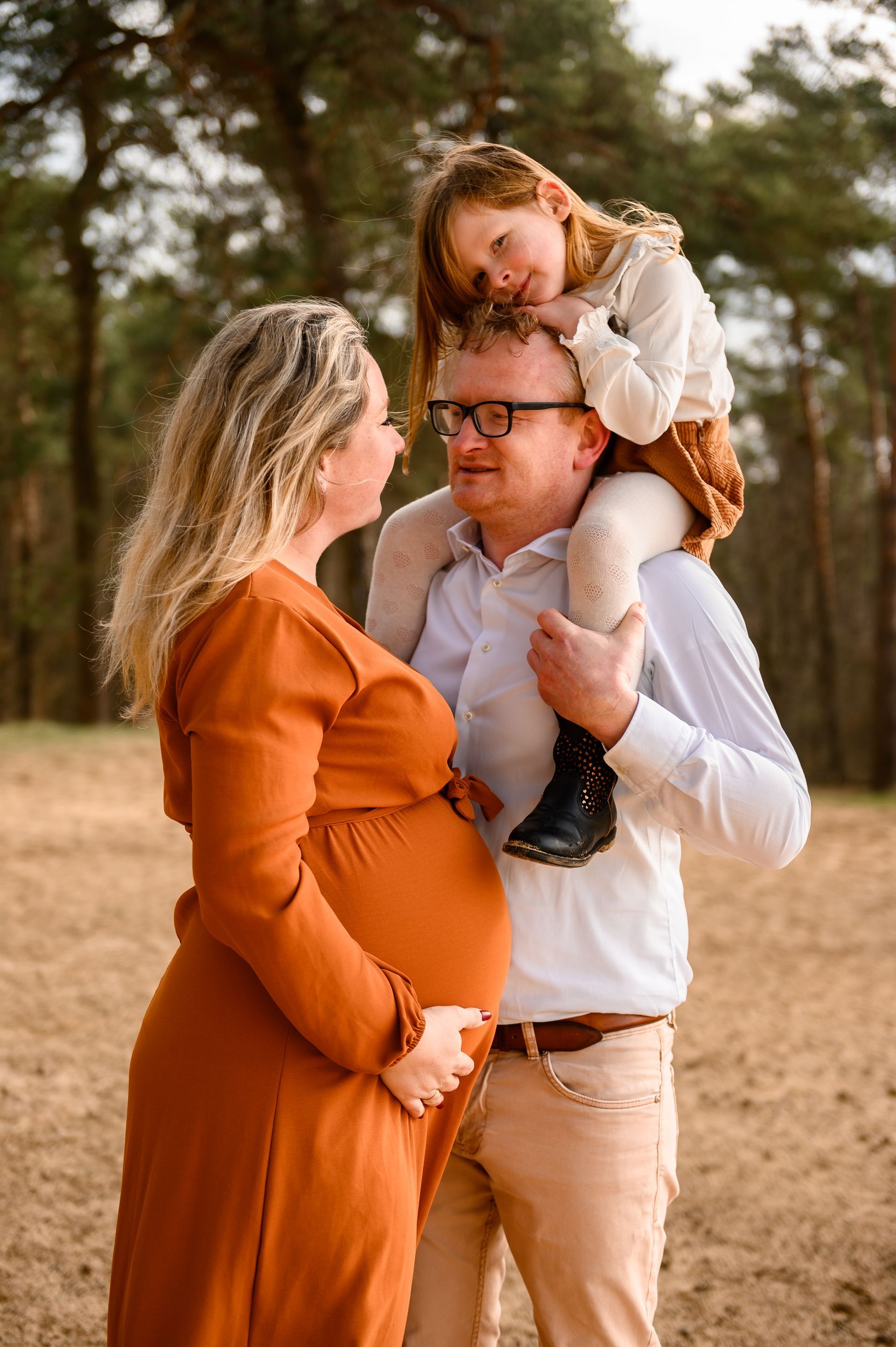 Zwangere vrouw met familie buiten, houdt haar buik vast, haar man draagt ​​het kind op zijn schouders.