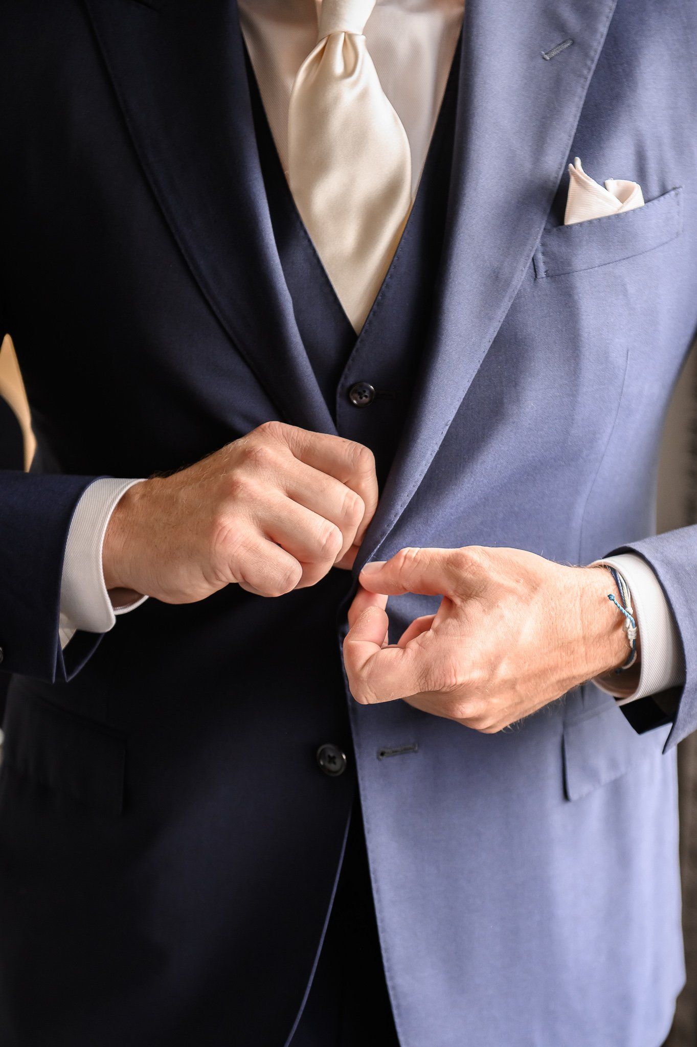 Een man knoopt de lichtblauwe blazer van een tweekleurig pak dicht. Hij draagt ​​een crèmekleurige stropdas, een pochet en een wit overhemd.