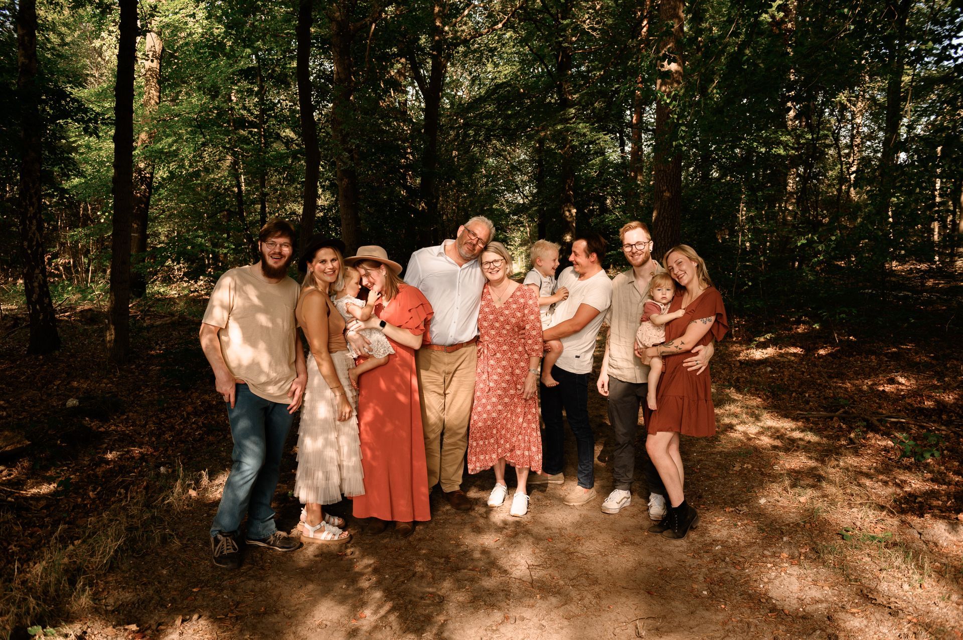 Een familiegroep poseert in een bos; zonnige dag. De mensen staan dicht bij elkaar.