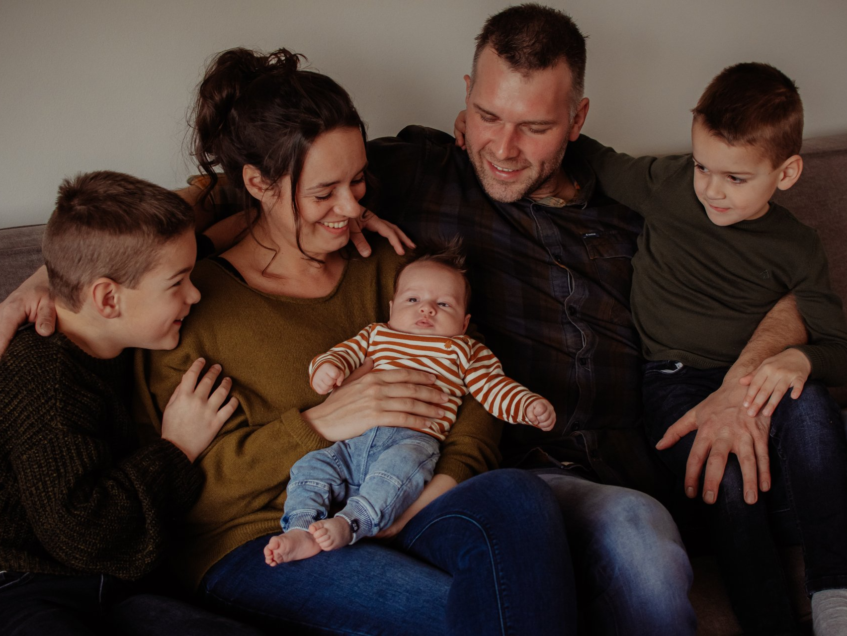 Een gezin van vijf zit op een bank; de ouders en drie kinderen kijken naar een baby.