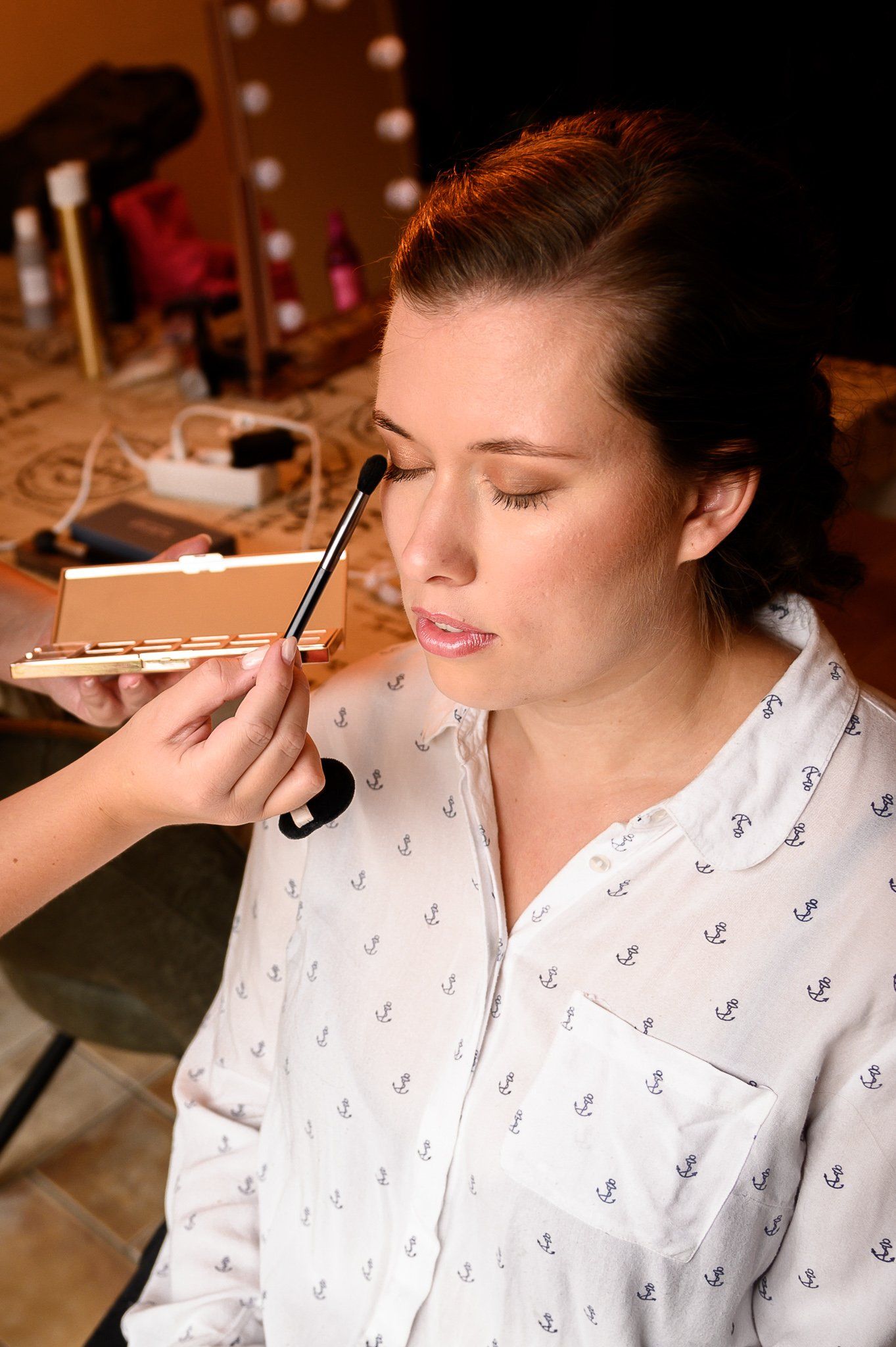 Een persoon krijgt oogmake-up aangebracht met een kwast, een lichtgekleurd shirt en een make-uppalet.