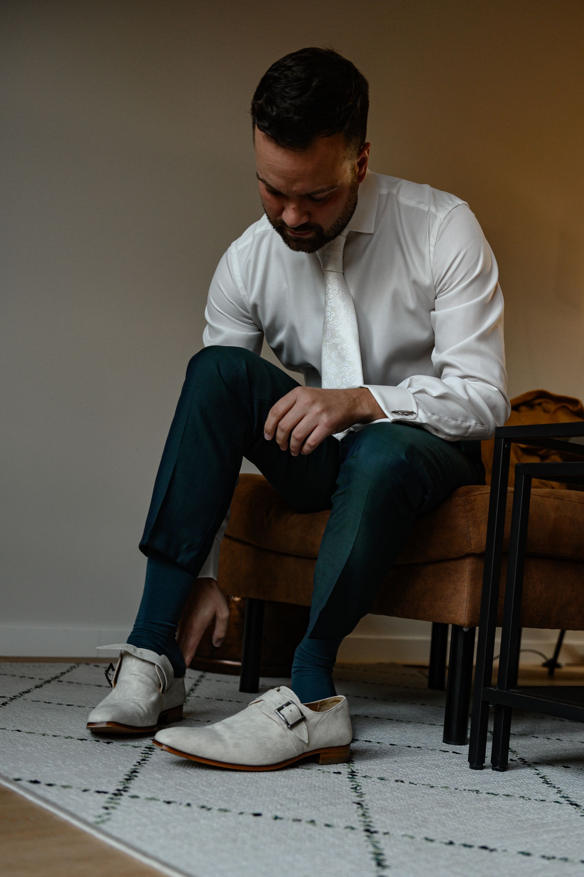 Een man zit en trekt zijn witte schoen recht. Hij draagt ​​een wit overhemd, een turquoise broek en donkerblauwe sokken.