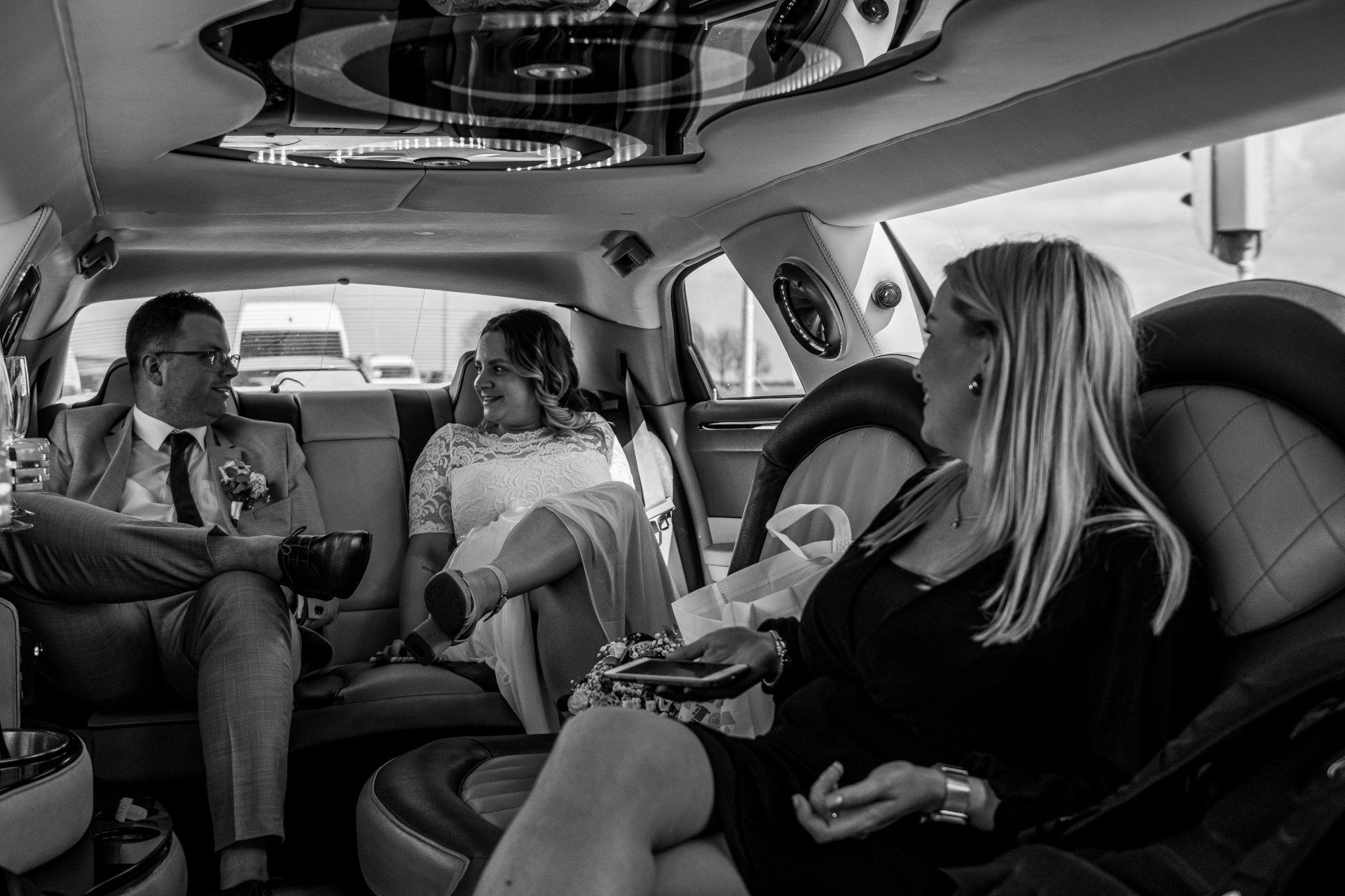 Bruid en bruidegom met een gast in een limousine. Ze glimlachen. Het interieur is licht.