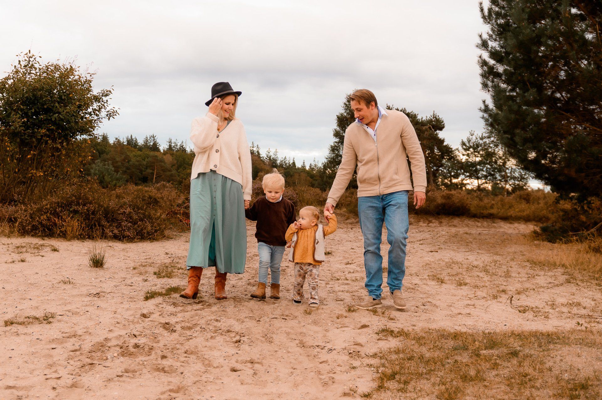 Een gezin van vier loopt hand in hand over een zandpad in een natuurlijke omgeving.