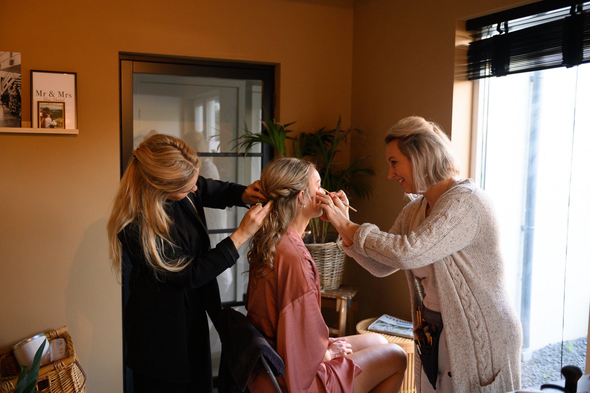 Twee vrouwen verzorgen het haar en de make-up van iemand. Warm verlichte kamer; persoon in badjas.