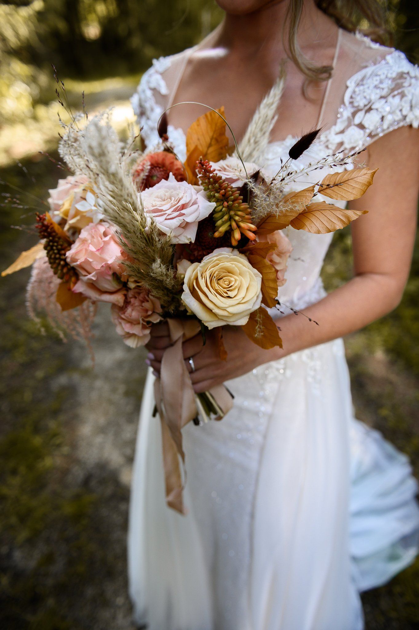Bruid in een witte jurk met een boeket perzik- en goudkleurige bloemen, buitenlocatie.