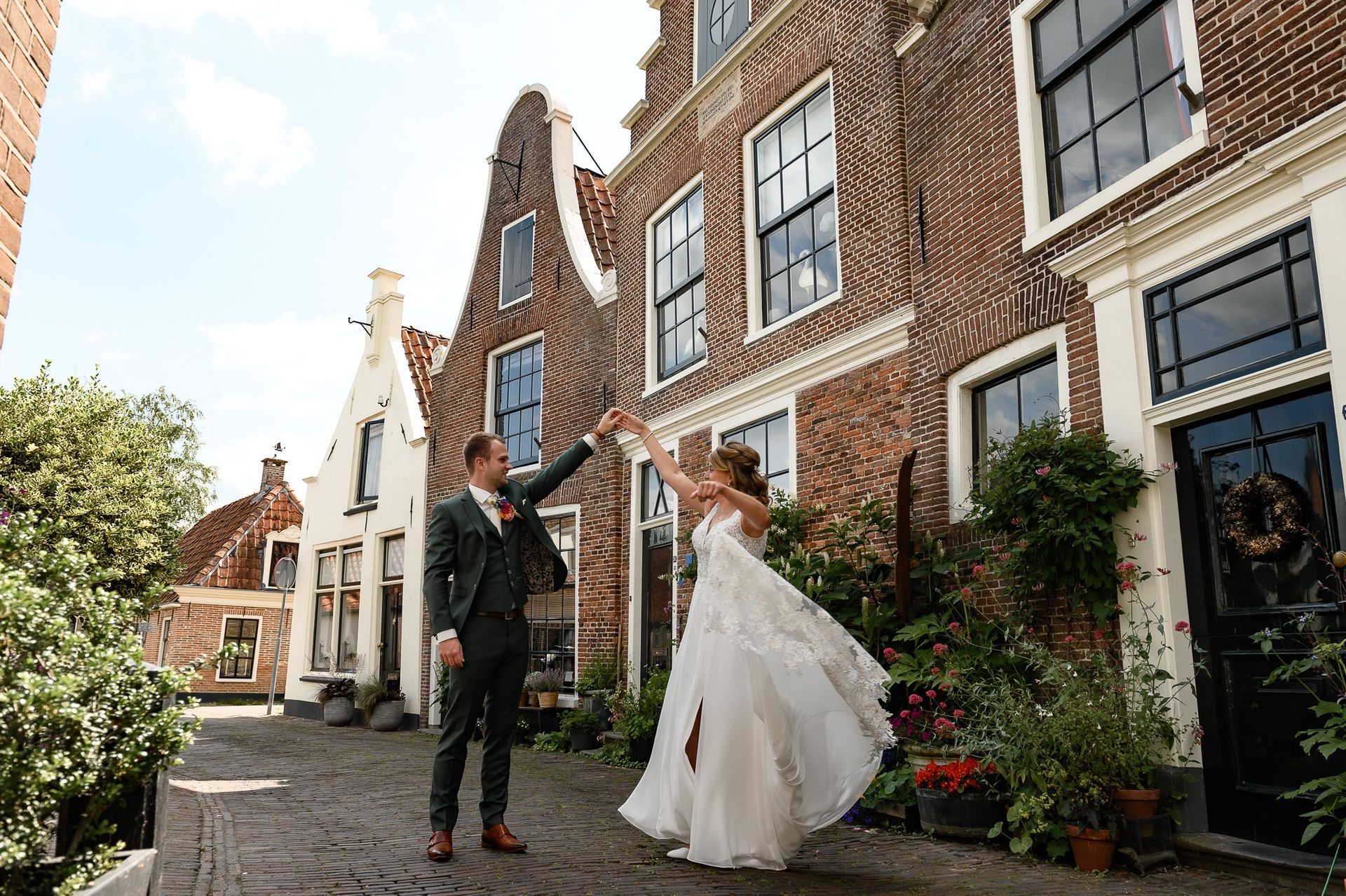 Een stel draait rond in een straat met kinderkopjes, met op de achtergrond historische bakstenen gebouwen. Zij draagt ​​een witte jurk, hij een pak.