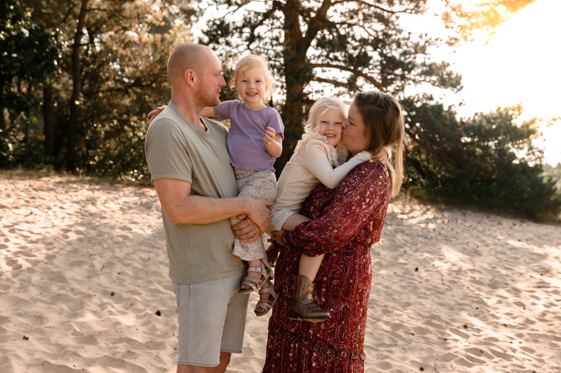 Een gezin op een zandstrand; de vader houdt een kind vast, de moeder een ander, iedereen lacht.